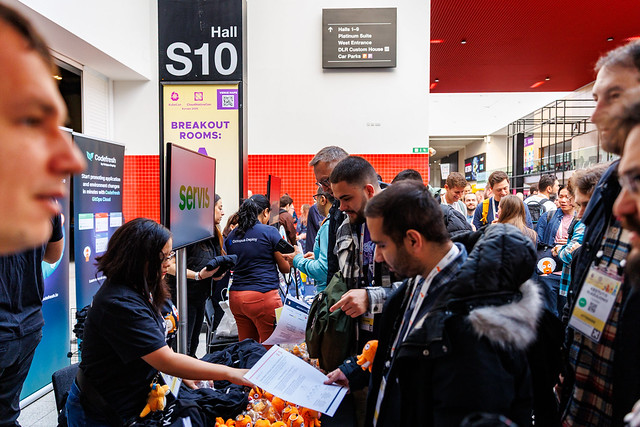 People talking at booths at a previous Kubecon event. If you want to know how to prepare for Kubecon, booth strategy is key.